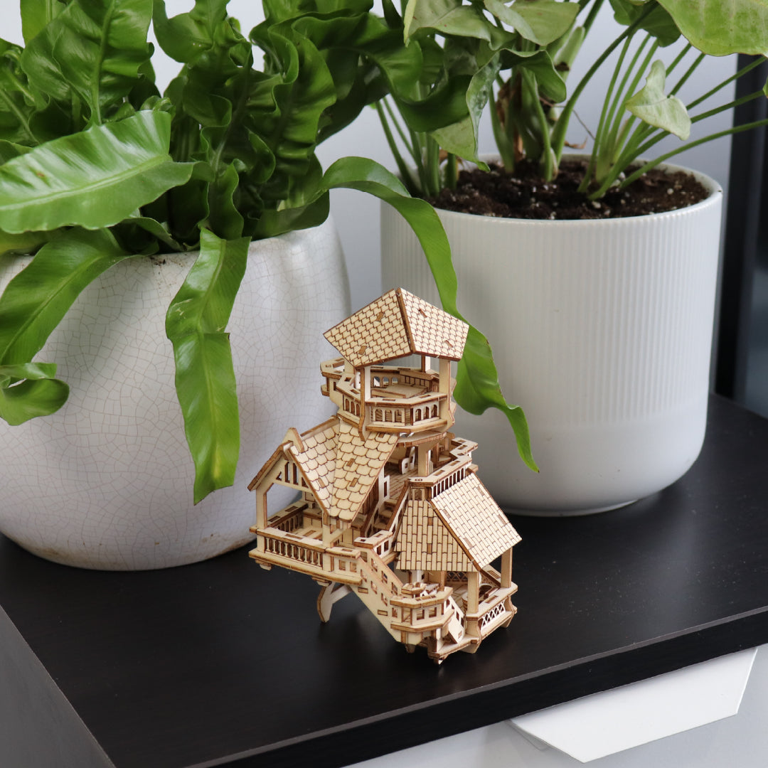 Tiny Treehouses 3D Puzzle Wooden model of a Tiny Treehouse on a black surface with potted plants in the background