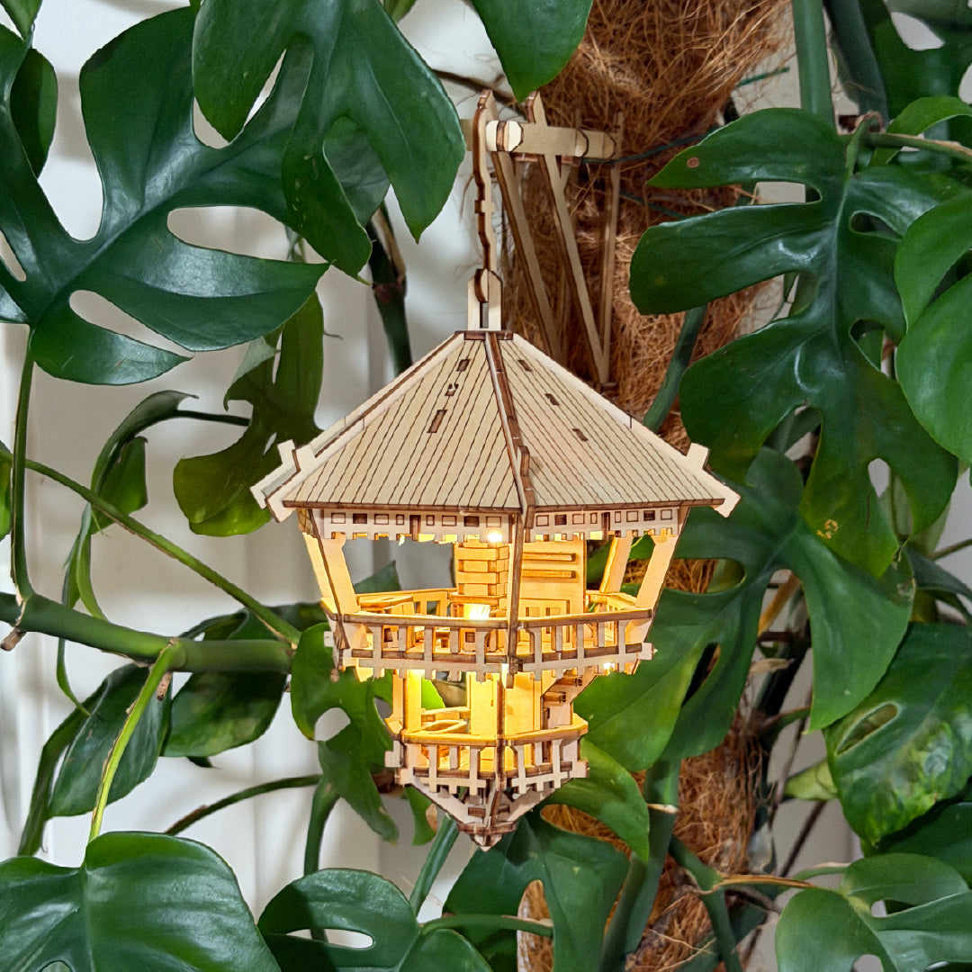 Tiny Treehouses 3D Puzzle Wooden model with a light inside, hanging among green leaves