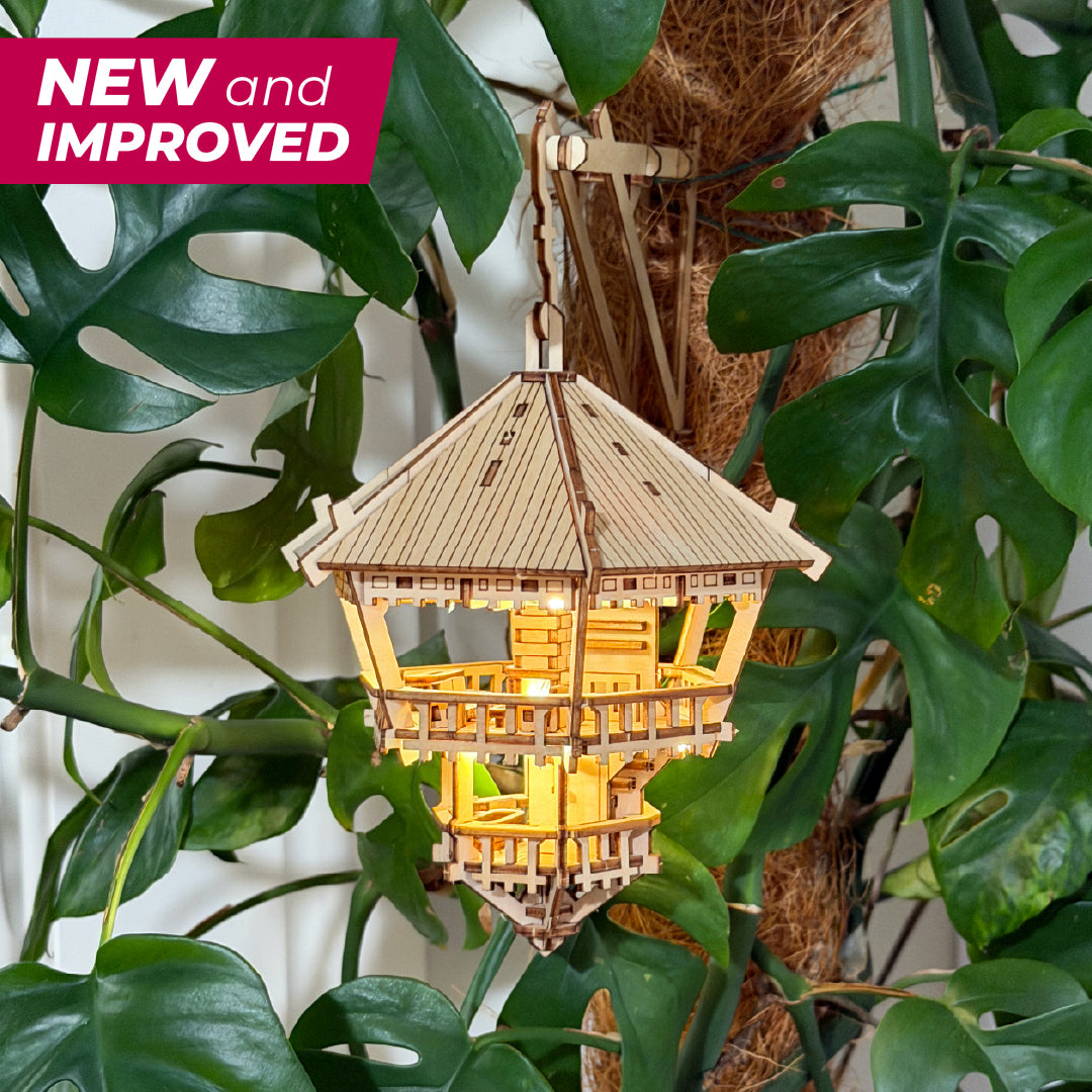Tiny Treehouses 3D Puzzle Wooden model with a warm glow, hanging among green leaves, with &