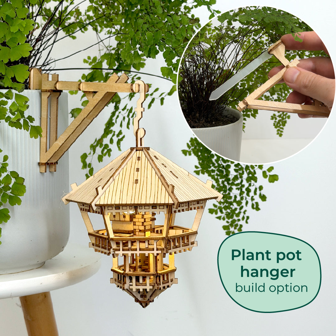 Tiny Treehouses 3D Puzzle Wooden plant pot hanger with a small inset showing a hand using a tool to plant a seedling.