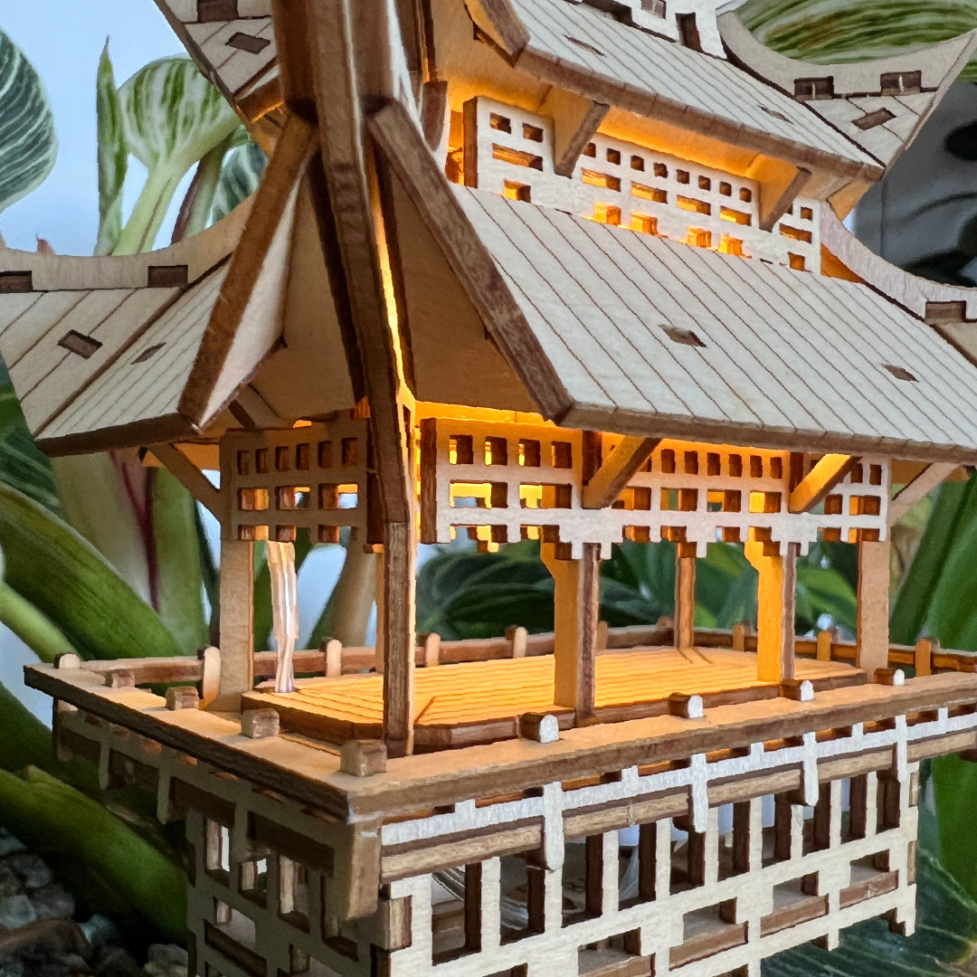 Tiny Treehouses 3D Puzzle Wooden Tiny Treehouse 3D Puzzles model of a traditional Japanese structure with glowing interior, surrounded by green leaves.