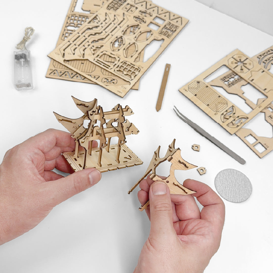 Tiny Treehouses 3D Puzzle Hands holding Tiny Treehouse 3D Puzzles wooden puzzle pieces with laser-cut designs on a white surface.