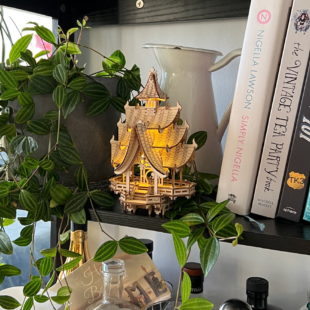 Tiny Treehouses 3D Puzzle Wooden pagoda Tiny Treehouse 3D Puzzle model with lights on a shelf with books and plants